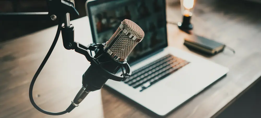 Photo of a podcast mic set up with a laptop on a table in the background.