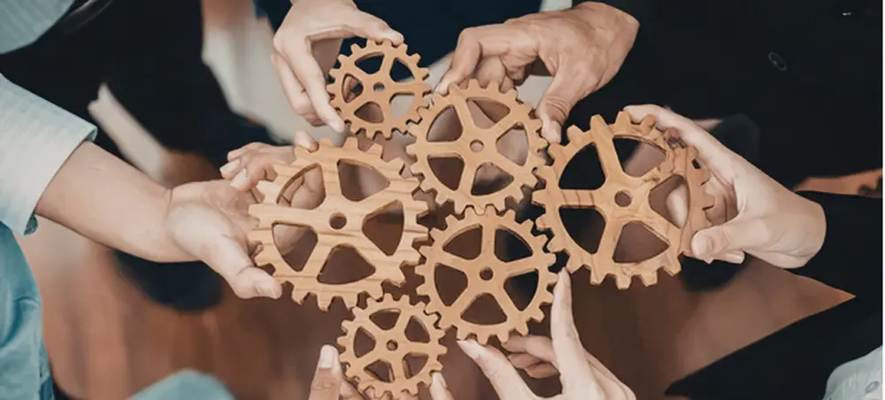People holding wooden gears together to indicate a system.