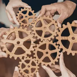 People holding wooden gears together to indicate a system.